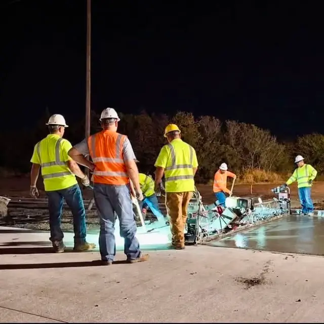 Crew in safety vests finishing concrete at night under work lights